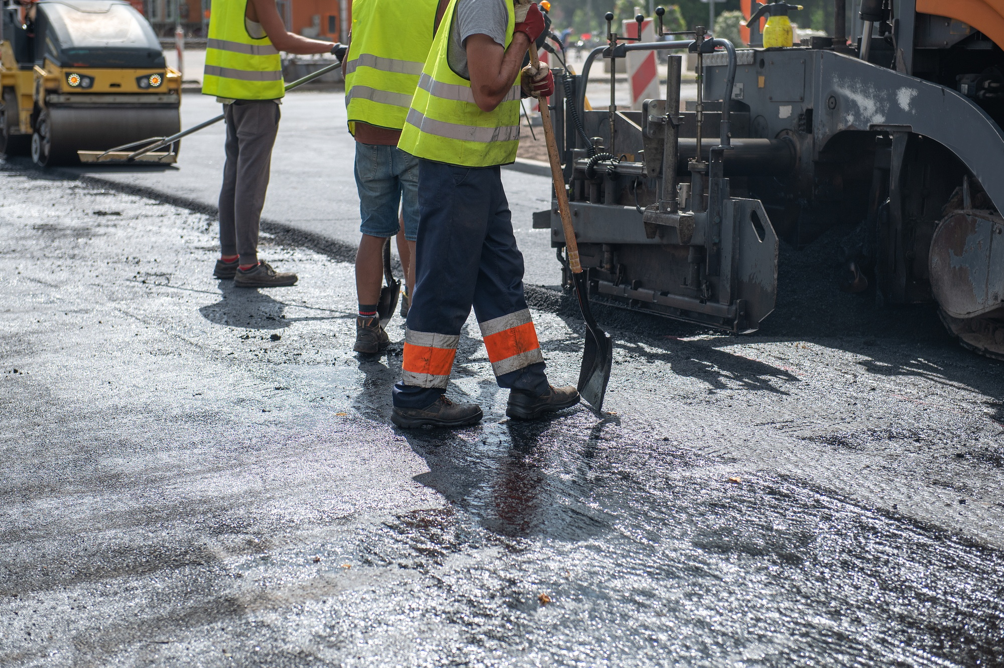 Workers operating asphalt paver machine during road construction and repairing works